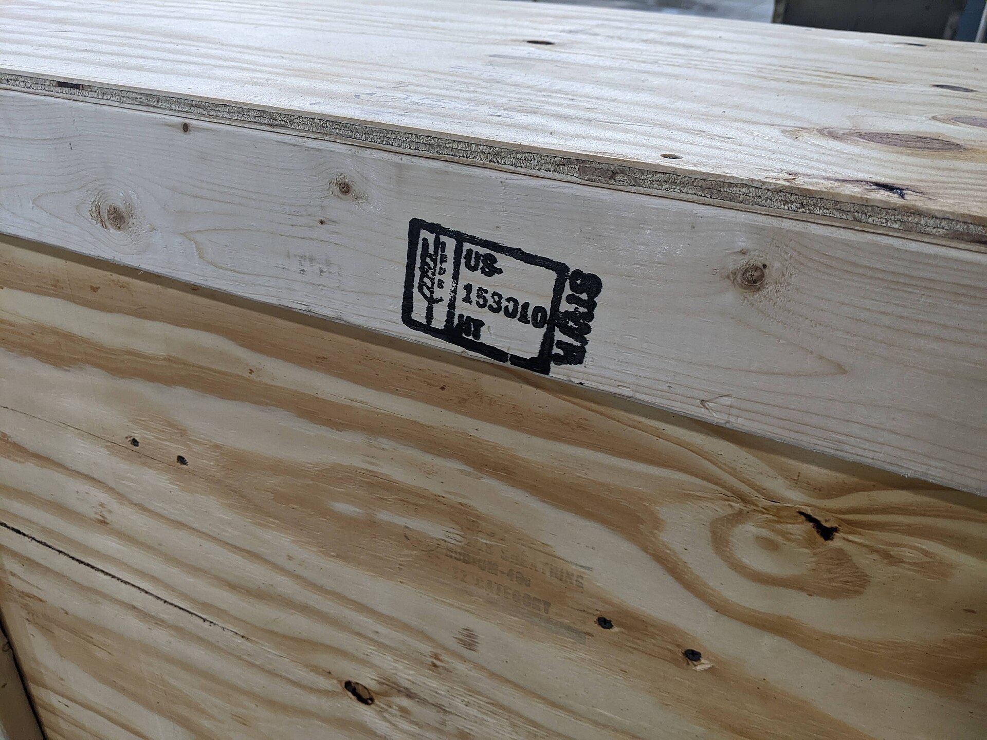 Wooden export crate photographed on edge with a black ISPM 15 certification stamp visible on the plywood panel